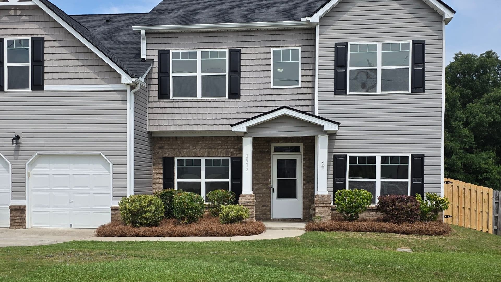 Fresh pine straw installed around foundation shrubs at a two-story home